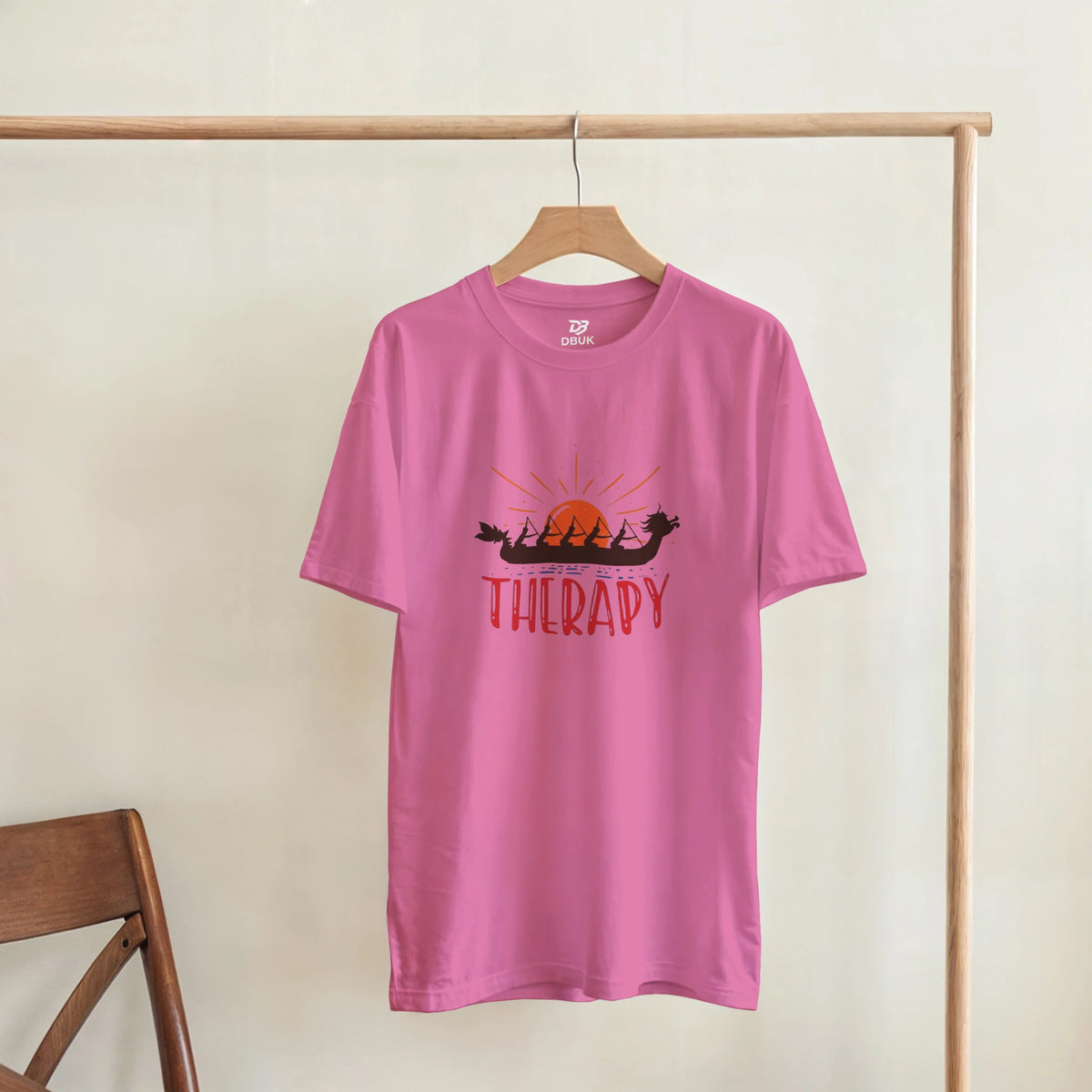 Azalea pink unisex T-shirt hanging on a hook with dragon boat "THERAPY" graphic