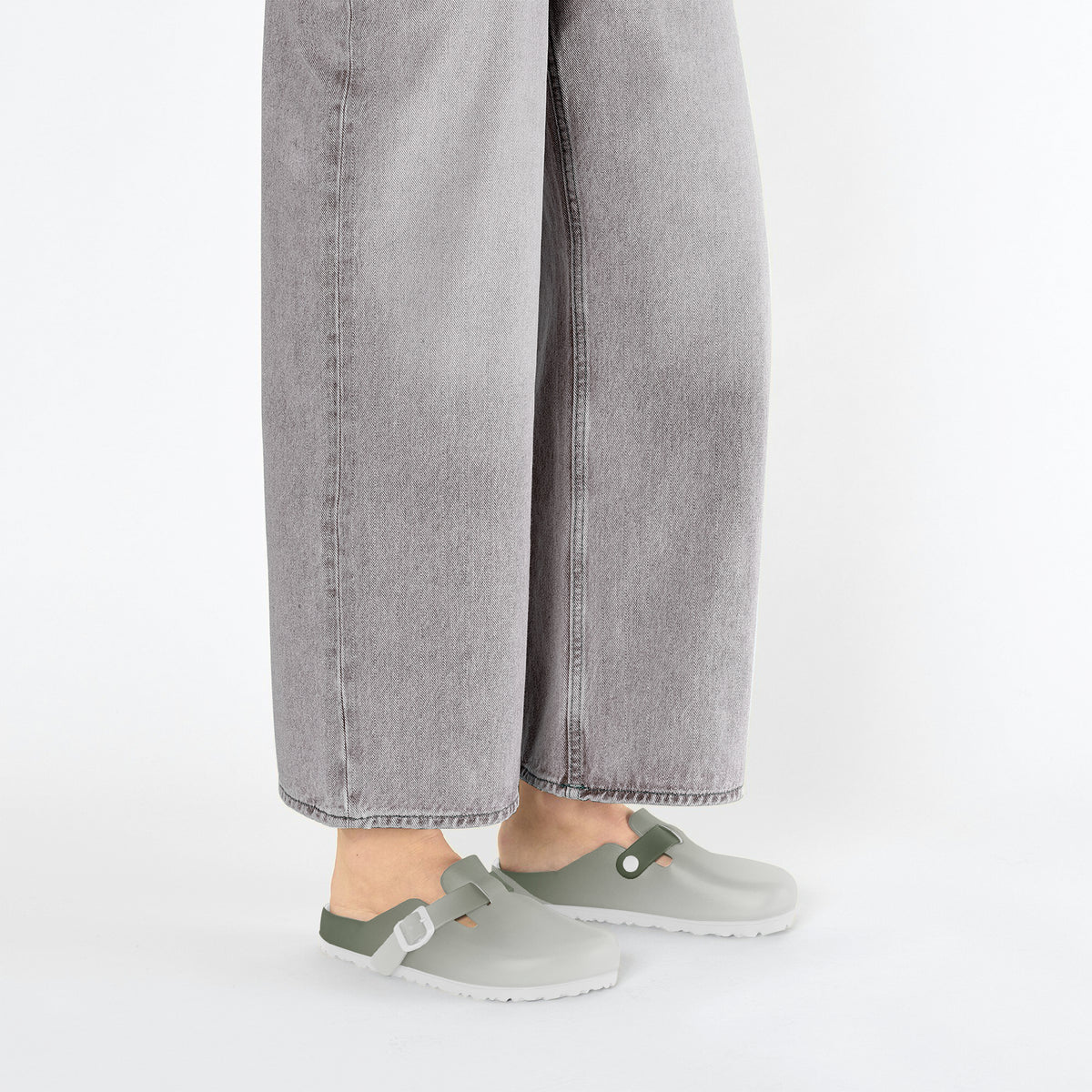 Feet wearing light gray EVA slip-on clogs with green accents and side buckle straps
