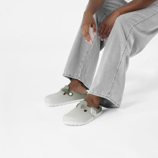 Pair of slip-on clogs with green heel trim and adjustable side straps on feet