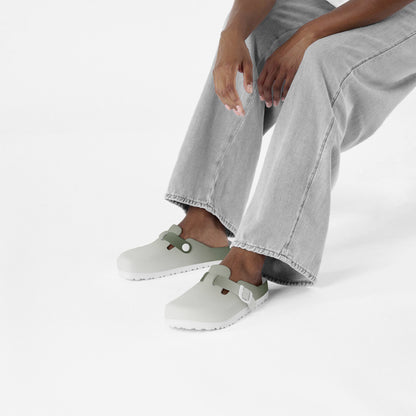 Pair of slip-on clogs with green heel trim and adjustable side straps on feet