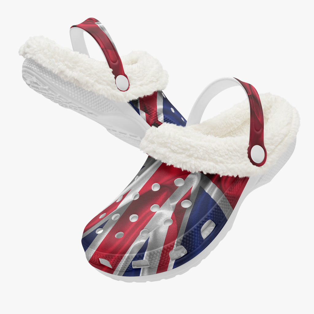A pair of white clog-style slip-on shoes with fluffy white faux-fur trim and red-and-blue strap details, featuring a Union Jack flag pattern on the uppers, shown on a light gray background.