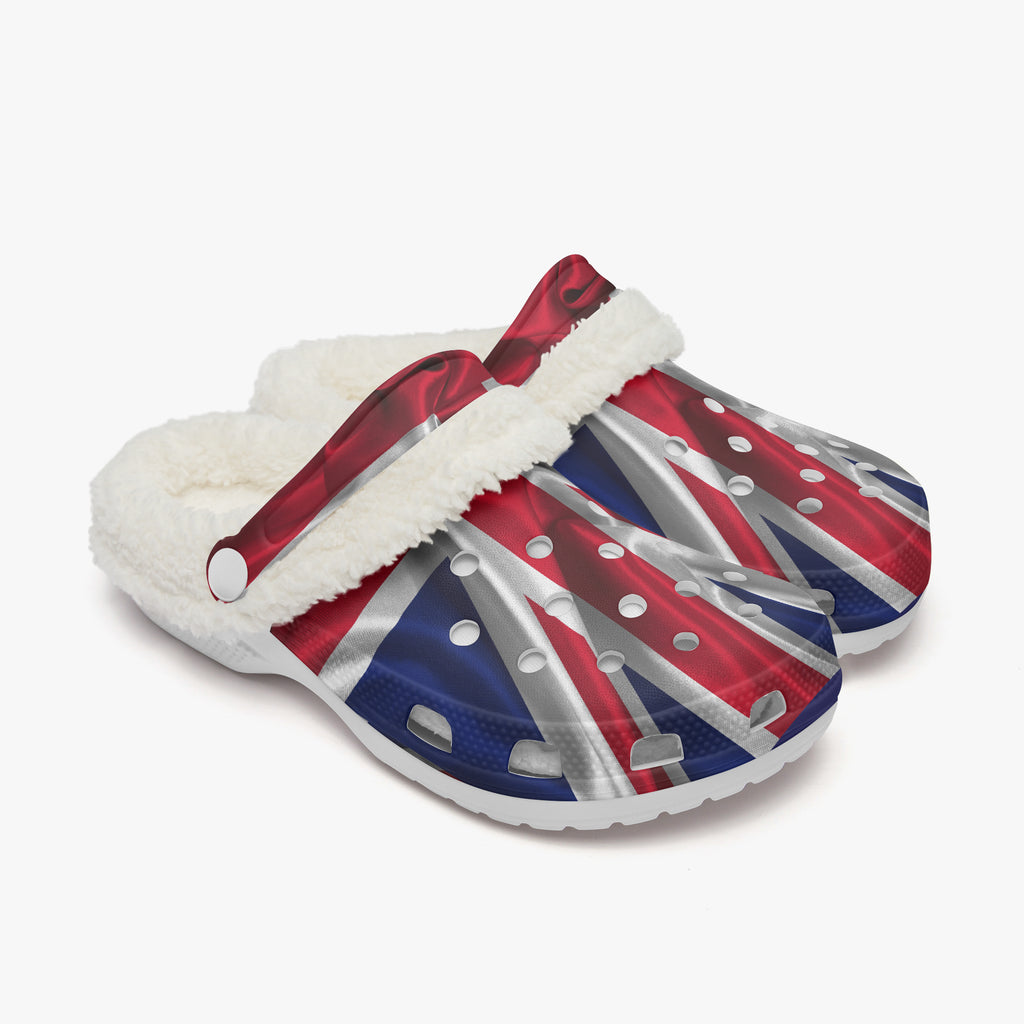 A pair of clog-style slippers featuring a Union Jack flag print in red, white, and blue, with a white faux-fur trim and a red strap across the top, shown on a light gray background.