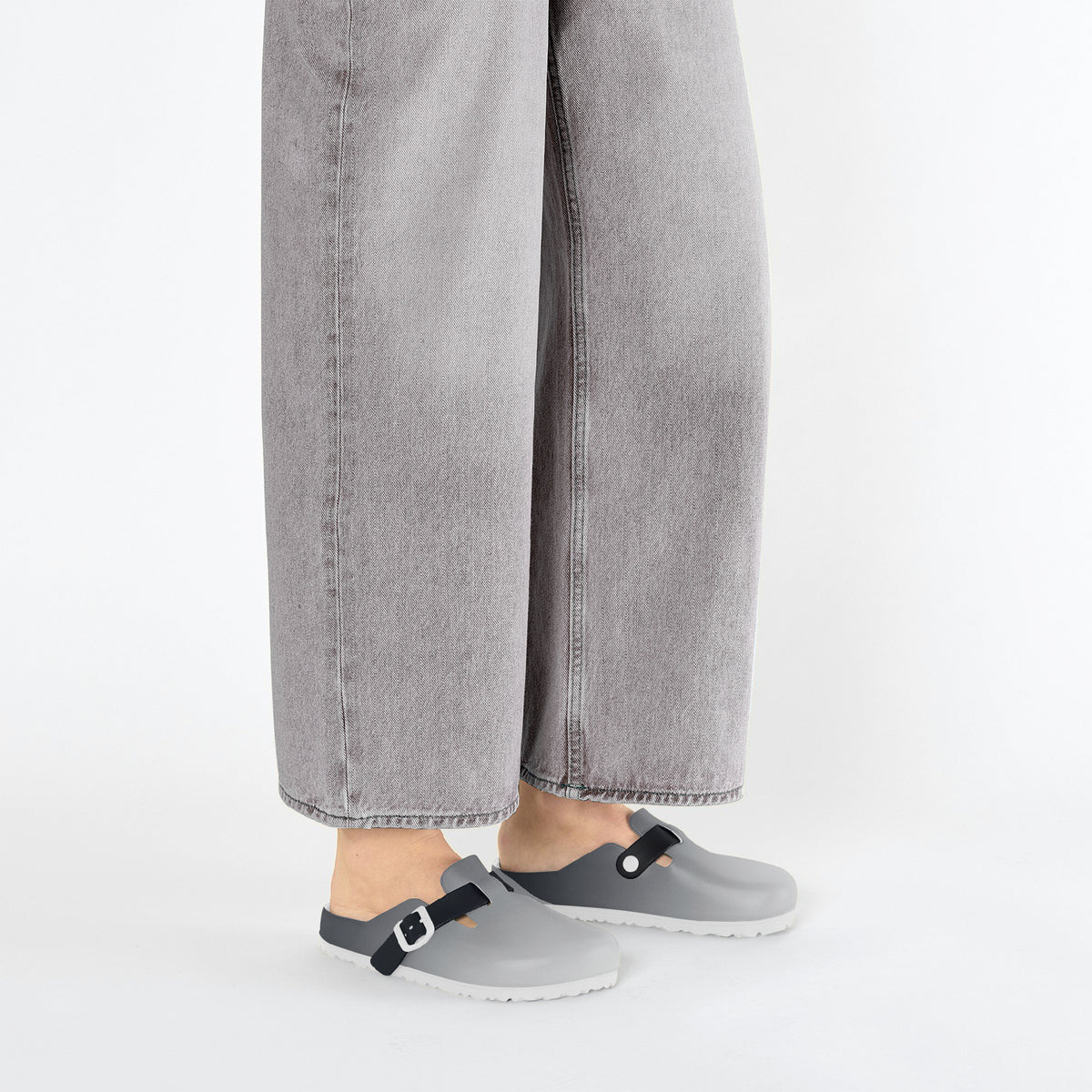 Grey slip-on clogs with black strap buckles under cuffed denim and white socks