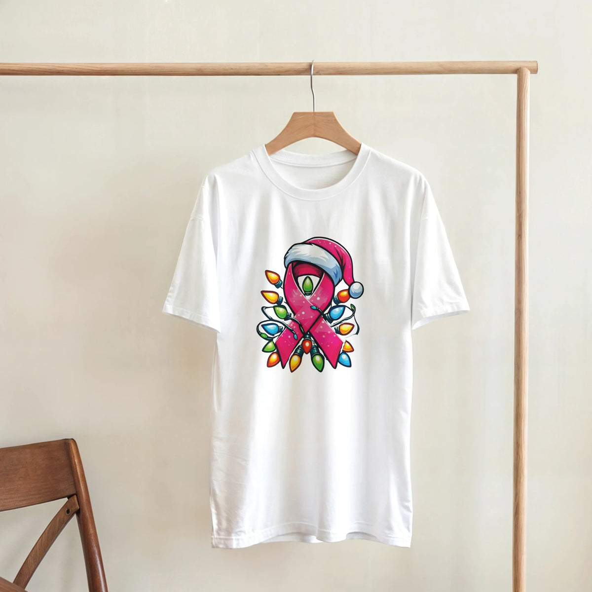 White crewneck T-shirt hanging with pink ribbon character graphic and colorful Christmas lights