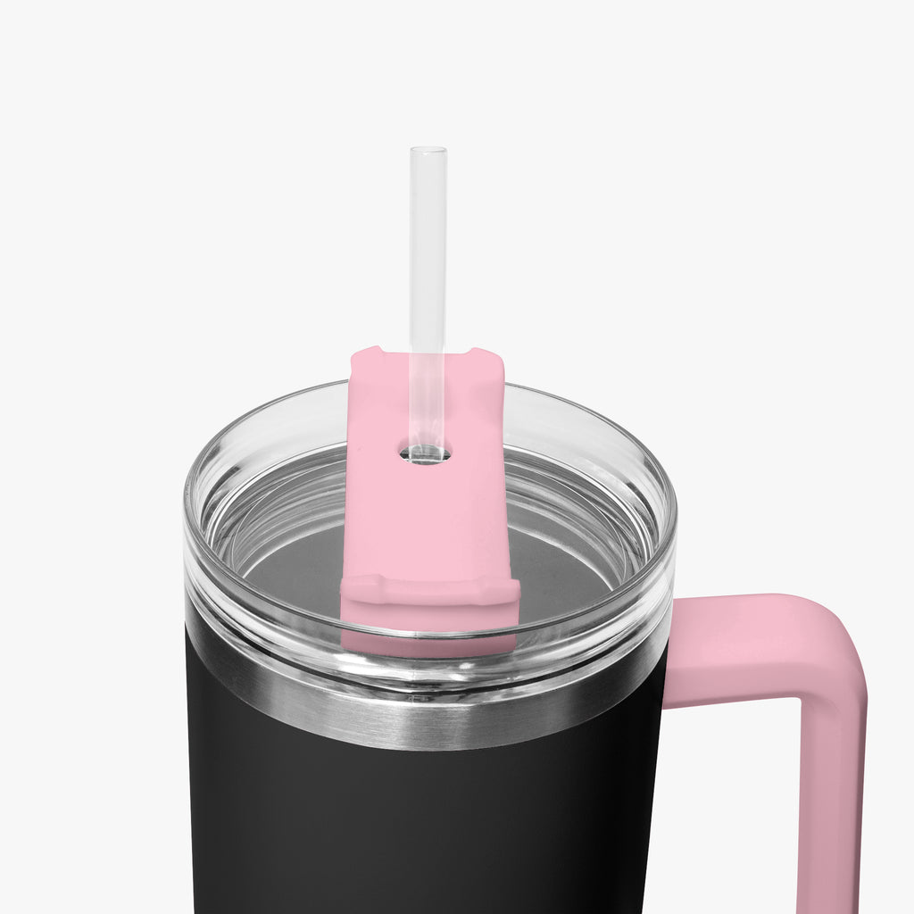 Close-up of a black insulated tumbler with a clear lid, pink straw cover, and pink handle on a light gray background.
