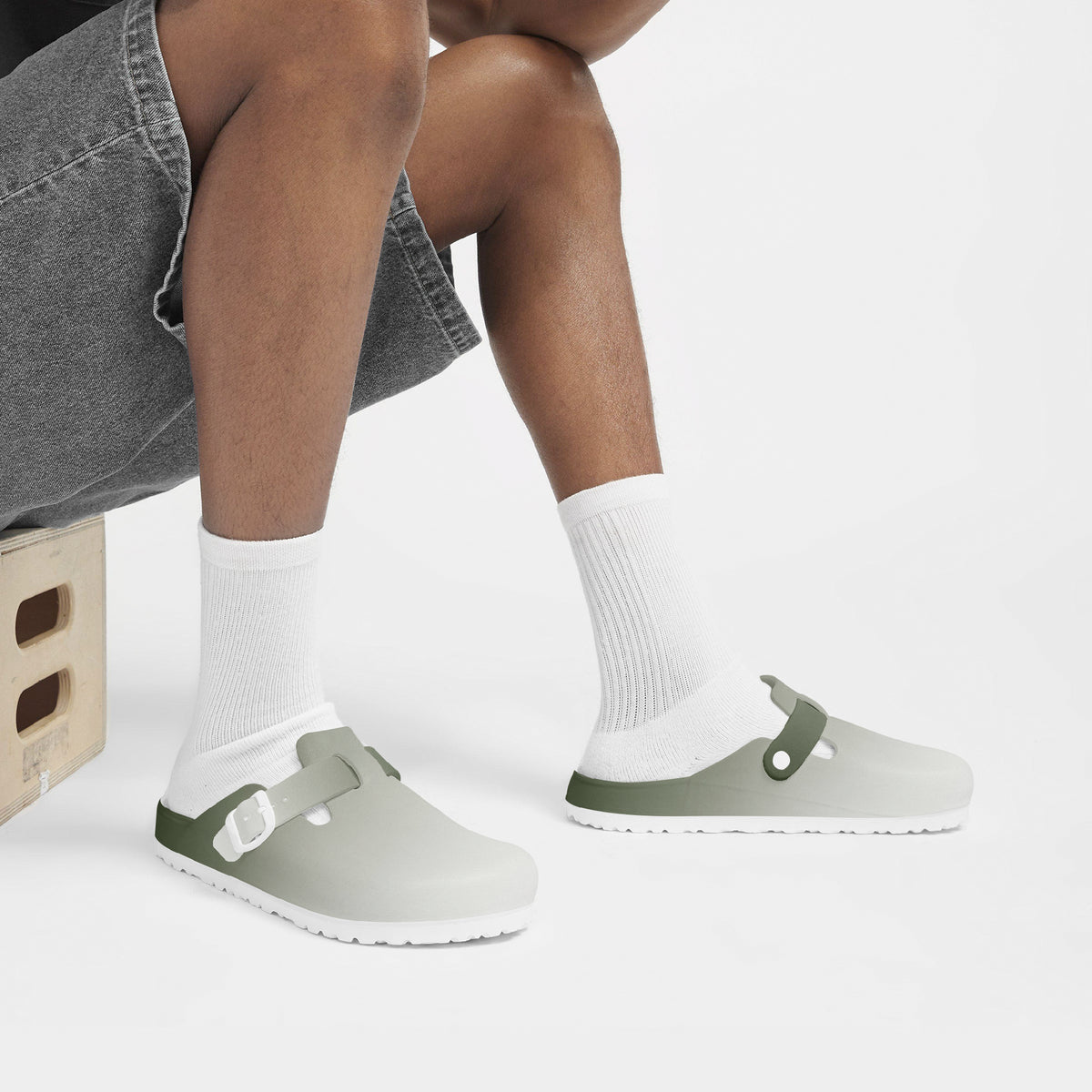 Cropped view of feet wearing light gray EVA clogs with green straps and tread sole