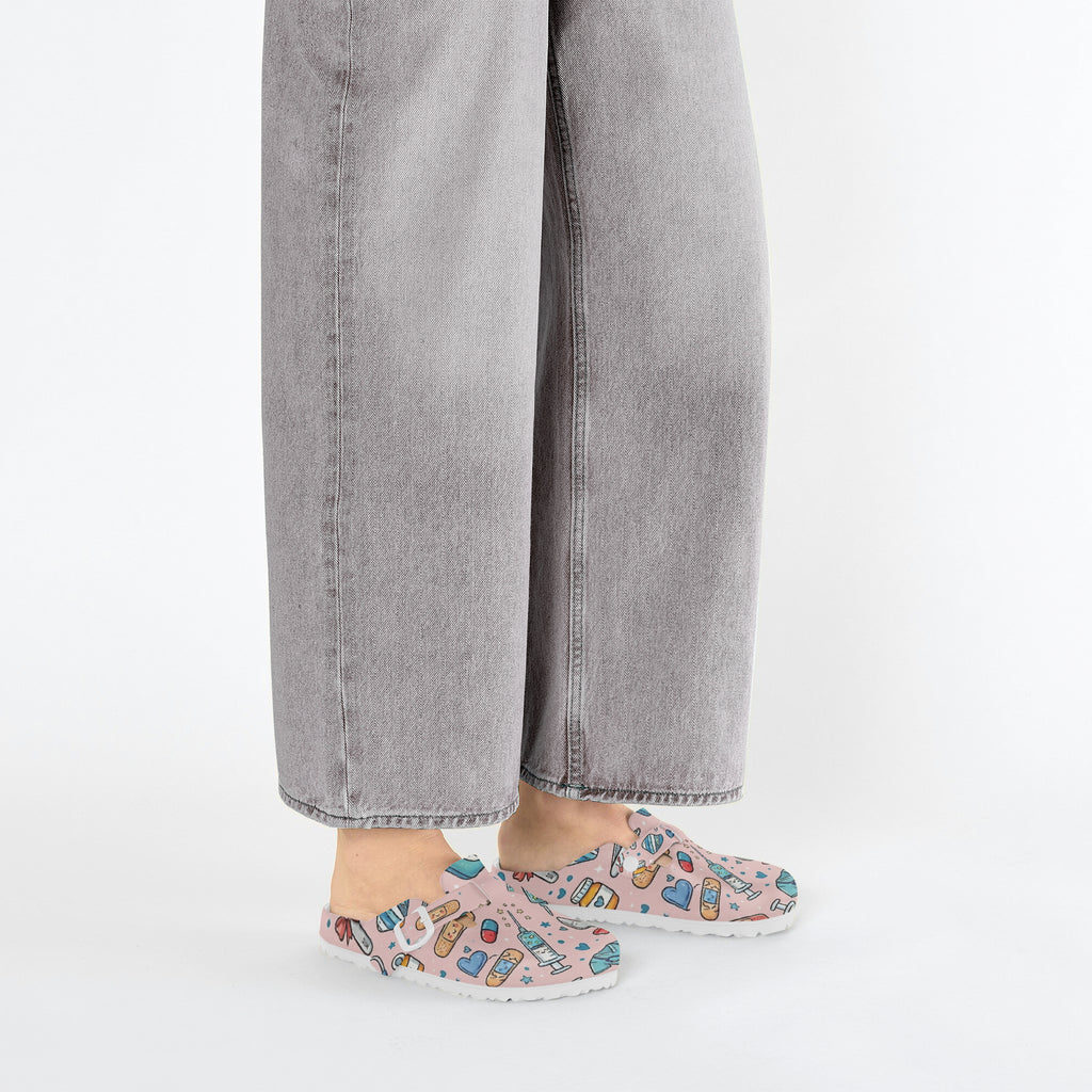 Pink medical doodle clogs worn with gray jeans, side view on white background