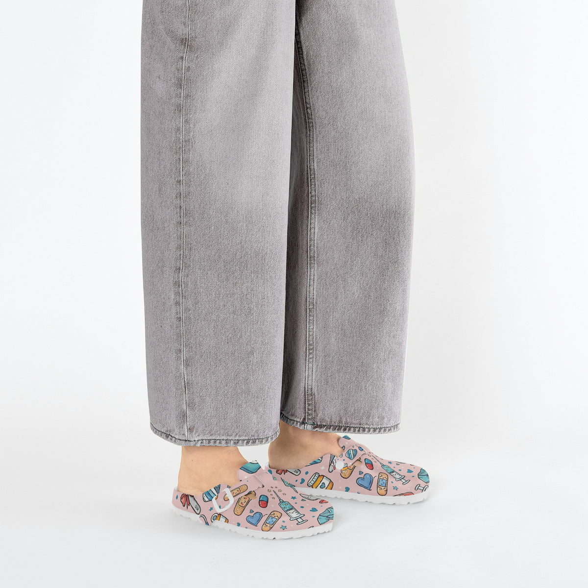 Pink medical doodle clogs worn with gray jeans, side view on white background