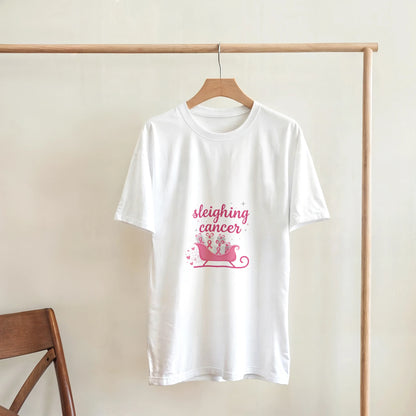 White cancer support T-shirt hanging on a hanger, pink “sleighing cancer” sleigh graphic