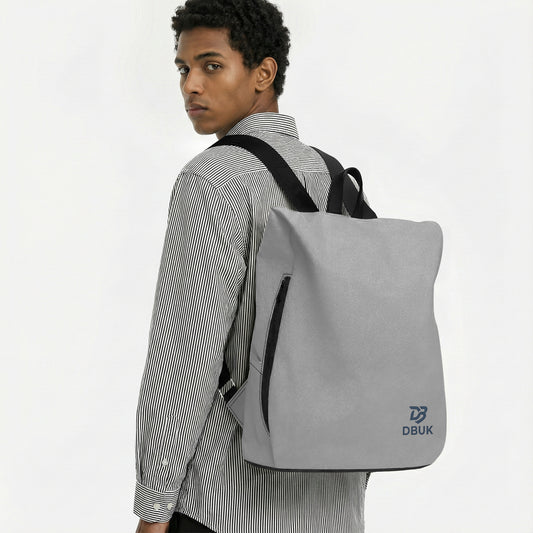 Light gray canvas backpack worn with black straps, front zip panel and DBUK logo